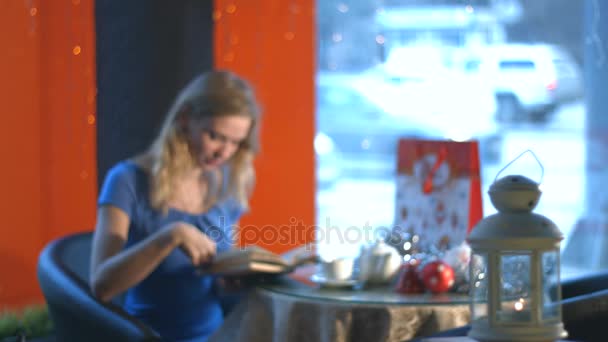 Κορίτσι με ένα βιβλίο σε ένα καφέ. — Αρχείο Βίντεο