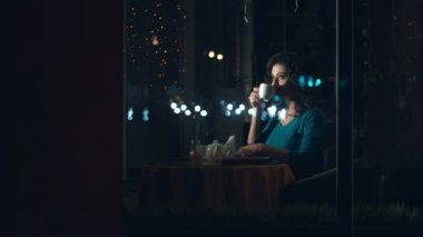 Sevimli kadın bir kafede. Ağır çekim. Güzel bir kadın cam ve içecek çay veya kahve arkasında bir kafede oturuyor. Kentsel ulaşım ve trafik cam yansıtır.