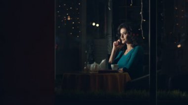 Bir kafede bir akıllı telefon olan kadın. Ağır çekim. Güzel bir kadın cam arkasında bir kafede oturuyor ve telefonda iletişim kurar. Kentsel ulaşım ve trafik cam yansıtır.