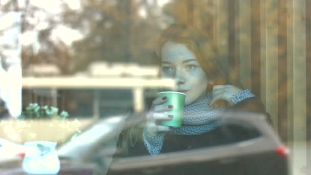 カフェで美しい少女 スローモーション 若いきれいな女の子がガラスの背後にあるカフェで座っていると コーヒーを飲みます ガラスは 都市交通の交通を反映しています — ストック動画