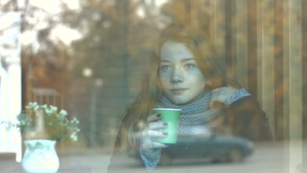 咖啡馆里的漂亮女孩慢动作一个年轻漂亮的女孩坐在咖啡馆后面的玻璃和喝咖啡 玻璃反映城市交通 — 图库视频影像