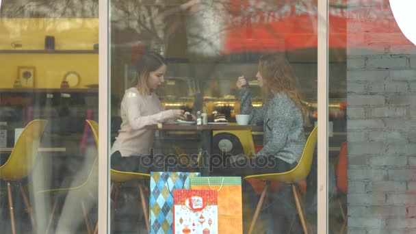 カフェで二人の女の子 スローモーション 人の女の子は ガラスの背後にあるカフェで座っています 彼らは ケーキとお茶を飲むし — ストック動画