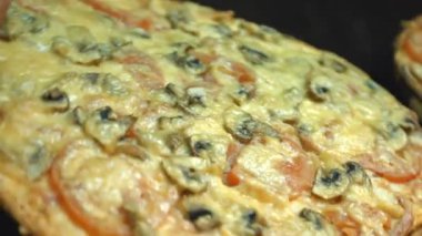 İki pizza döndürün. Yakın çekim. Yatay (soldan sağa) pan. Karanlık bir arka plan üzerinde kurullarında pizzalar döndürmek.