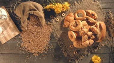 Tatlı ekmek buğday unu ile yapılan. Üstten Görünüm. Ağır çekim. Kamera olduğunuz yulaf demet, çeşitli çörekler, tahıl ve un bir çanta bir eski ahşap masa üzerinde taşır. Bir yığın buğday kulak masaya koy yapıldı..