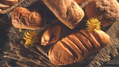 Ekmek, buğday, un ve çiçekler ile natürmort. Yakın çekim. Üstten Görünüm. Yatay (sağdan sola) pan. Ekmek, kucak dolusu buğday kulaklar, tahıl bir torba, bir bardak un eski masa.