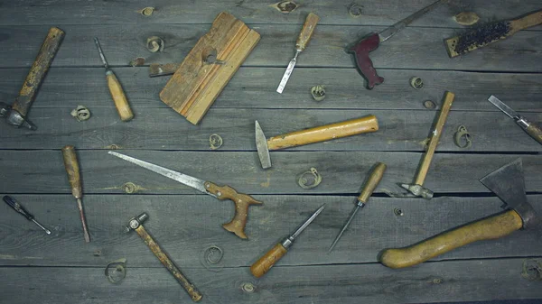 Old hand tools. Top view. On the table are mixed work tools (screwdrivers, chisels, hand saw, hammers, ax, awl, metal brush, jointer) of the 60s, 70s, 80s with wooden handles.