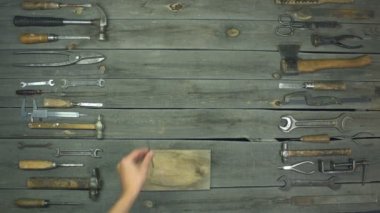 Ahşap ve metal için aletler. Stop-motion animasyonu. Üst manzara. Bir erkek eli masaya çivi ve çekiç koyar. Çekiç çiviye çarptı. Sonra el çekici kaldırır. Masanın üzerinde ahşap ve metal işlemek için çeşitli metal ve marangozluk aletleri bulunur..