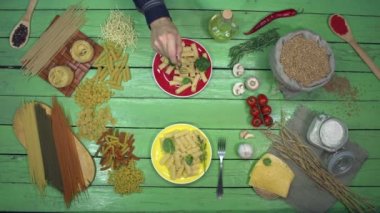 Ispanaklı renkli tabaklar üzerinde makarna tatmak. Üst Manzara. Yeşil masa sol tarafta birçok çeşit kuru makarna ve hamura bölünmüş durumda ve sebzeler, kiraz domatesleri, peynir, aroma ve mantarlar sağ tarafta..