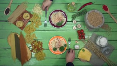 Eko masasında renkli tabaklarda spagetti tatmak. İki kişi akşam yemeğinde domates soslu spagetti yer. Lezzetli geleneksel İtalyan yemeği. Yakınlarda yağ, sebze, değişik türde kuru makarna ve mantarlar var..