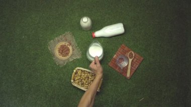 Fıstık sütü. Üst Manzara. Ağır çekim 2x. Çimlerde fıstık sütü ve fıstık. Bir erkek eli sürahiyi alır ve bardağa süt döker. Diğer elin bardağı alır..
