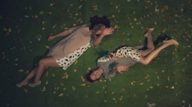 Çimlerin üzerinde iki kız. Ağır çekim 2x. Üst tabaka. Beyaz ve beyaz kızlar sarı yaprakların arasında çimlerin üzerinde yatıyorlar. Kar yağışı hoşlarına gidiyor. İyi akşamlar. Kar yağıyor.