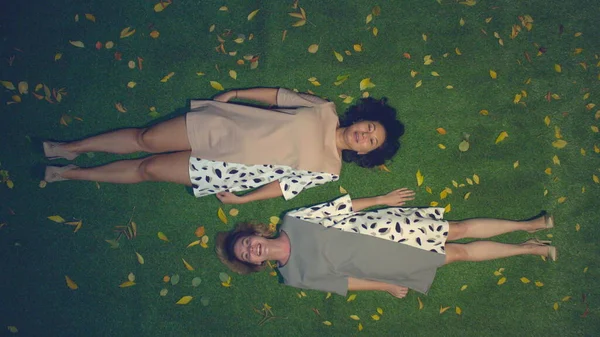 Çimlerin üzerinde iki kız. Üst Manzara. Asyalı ve beyaz kızlar sarı yaprakların arasında çimlerin üzerinde yatarlar. Neşeli bir şekilde sohbet edip gülüyorlar. İyi akşamlar..
