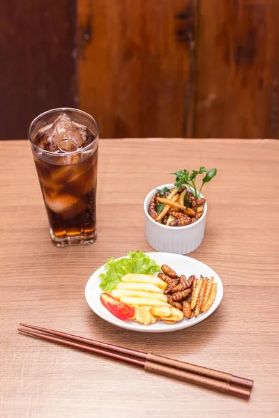 Insects - Wood worm, Silkworms fried insect, Tasty potatoes fries and chopsticks on white plate with wooden background.  Insects is preferable for the people of Cambodia and Thailand. Select Focus