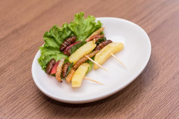 Insectos: gusano de madera, gusanos de seda fritos, papas fritas y palillos en un plato blanco con fondo de madera. Los insectos son preferibles para el pueblo de Camboya y Tailandia. Seleccionar enfoque — Foto de Stock