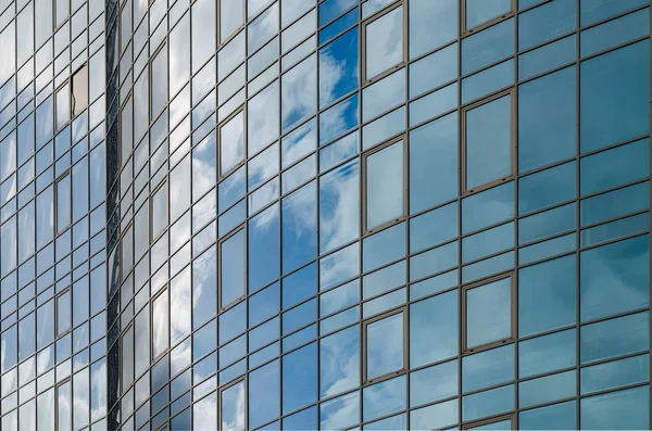 Skyscraper mirror glass surface reflecting cloudy sky, curvy surface