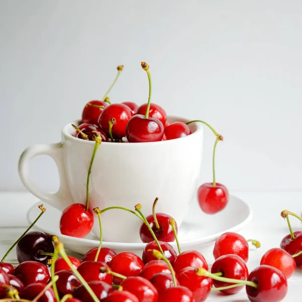 Ripe sweet cherries in a white cup on white wooden background, tasty and healthy dessert — Stock Photo, Image