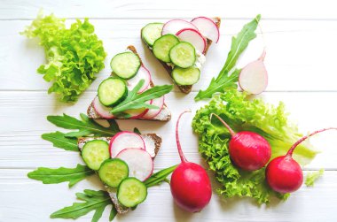 Sandviç buğday brown bread salatalık ile ve taze yeşil salata yaprakları Beyaz ahşap zemin üzerinde ile turp