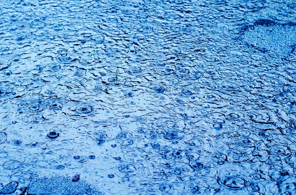 Gocce di pioggia sulla superficie di una strada in un giorno di pioggia, blu tonica — Foto Stock