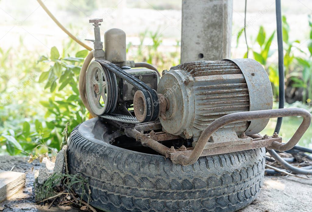 Old electric motor pumping machine on a black car wheel using for farming or gardening in the house with green background at summer sunrise. The idea for technology and facilities in agriculture.