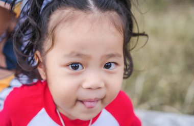 Dili dışarı fırlamış neşeli ve mutlu küçük bir kızın portresi. Yeşil yaz parkı arka planına sahip şirin Asyalı kadın çocuk pozları ve sağdaki metin için kopyalama alanı