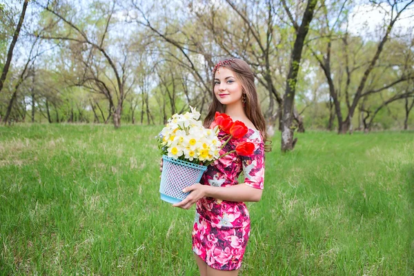 Очень красивая девушка с цветами в руках против солнца. Женщина с корзиной цветов в руках. Букет тюльпанов и нарцисса. Девушка с красивой худой фигурой — стоковое фото