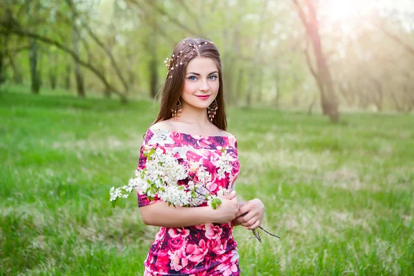 Красивая молодая девушка в ярком платье с цветами на естественном размытом фоне. Фотомодель в парке в ясный солнечный день. Женщина-флористка в цветочном саду — стоковое фото