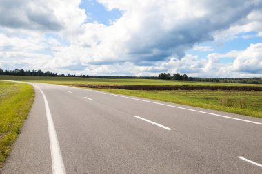 Uzun bir yol. Gökyüzü bulutları ve yeşil tarlalarıyla kır yolu manzarası
