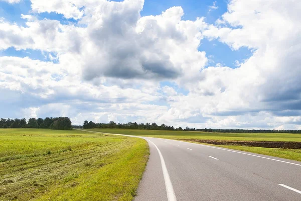 Long road. Country road landscape with sky clouds and green fields Royalty Free Stock Images