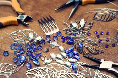 Tel, rhinestones ve kristalleri ile takı oluşturma işlemi. Masanın üzerinde çalışma araçları. El yapımı takılar. Üretim süreci içinde gelin bir tarak.