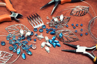 Tel, rhinestones ve kristalleri ile takı oluşturma işlemi. Masanın üzerinde çalışma araçları. El yapımı takılar. Üretim süreci içinde gelin bir tarak.