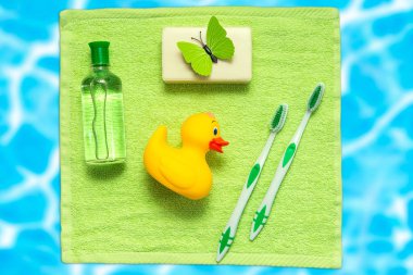 Banyo aksesuarları üzerinde yeşil bir havlu. Plastik ördek, diş fırçası, sabun ve losyon. Havuz su arka plan. Çocuk hijyen.