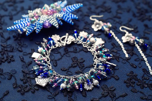 Set di gioielli. Bracciale con pendenti e perline in vetro e metallo. Sfondo strutturato con gioielli. Orecchini e fiori di perline . — Foto Stock