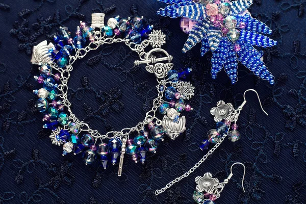 Set di gioielli. Bracciale con pendenti e perline in vetro e metallo. Sfondo strutturato con gioielli. Orecchini e fiori di perline . — Foto Stock