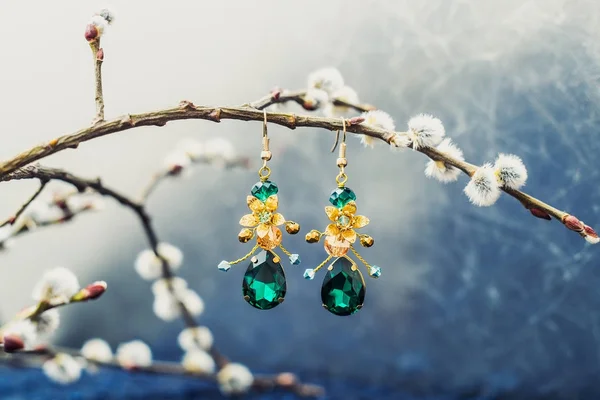 jewelry piece on simple branches background, earrings with golden flowers and rhinestones drops