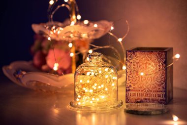 Rahat bir ev yapmak için çelenkler ve dekorasyonlar, tel üzerinde altın ışıklar, bir şamdan, bir vazo, bir kar saati topu ve ışıklarla aydınlatılmış diğer süslemeler..