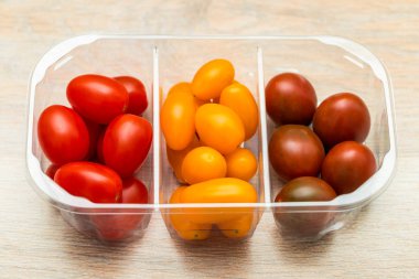 Cherry tomatoes in a plastic container, different varieties of yellow and red tomatoes
