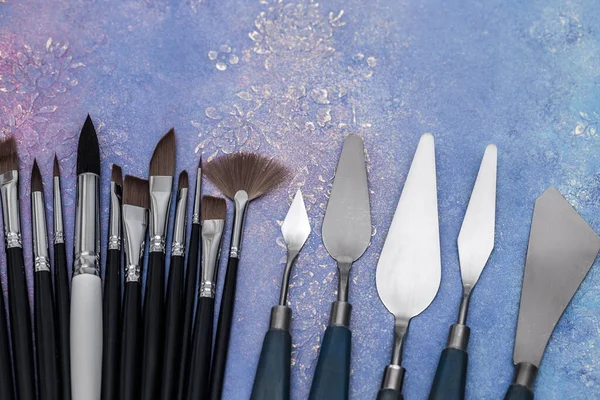 Artistic palette knives and drawing brushes, creative tools of various sizes and shapes on a worn painted Board