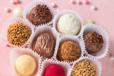 Tatlı çikolata şekerlemeleri ve pembe parlak arka planda şeker süslemeleri.