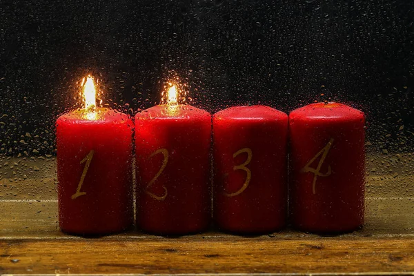 2 Advent. Advent candles in a row behind wet glass.