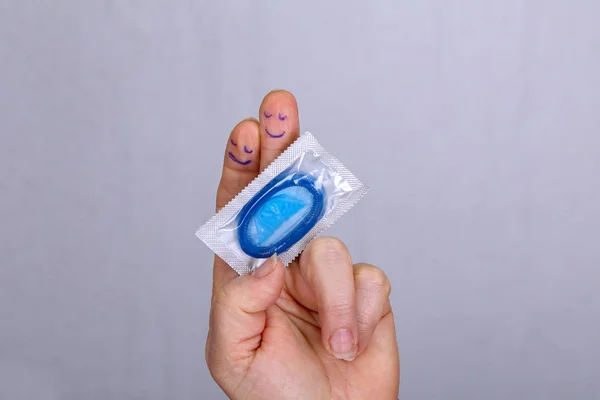 Hand with funny faces on fingers holds a condom
