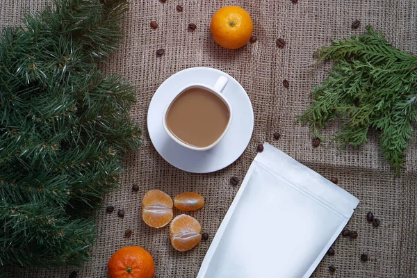 Mall av papper ekologisk väska för lagring av kaffe, te på en bakgrund av konsistens och en kopp cappuccino med tangeriner. Vakuumförpackning för jul och nyår närvarande — Stockfoto