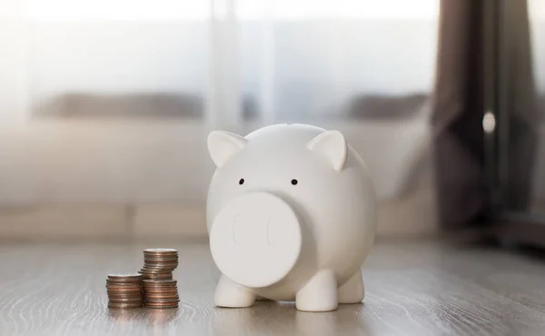 White piggy saving money with coin on wooden floor.