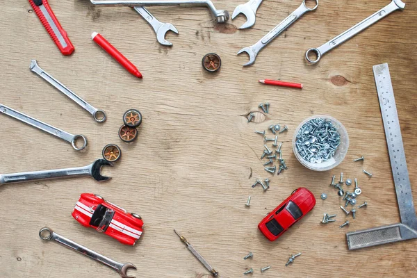 Flat lay of set of tools for car repairing on wooden background with contrast red toy cars. Top view.