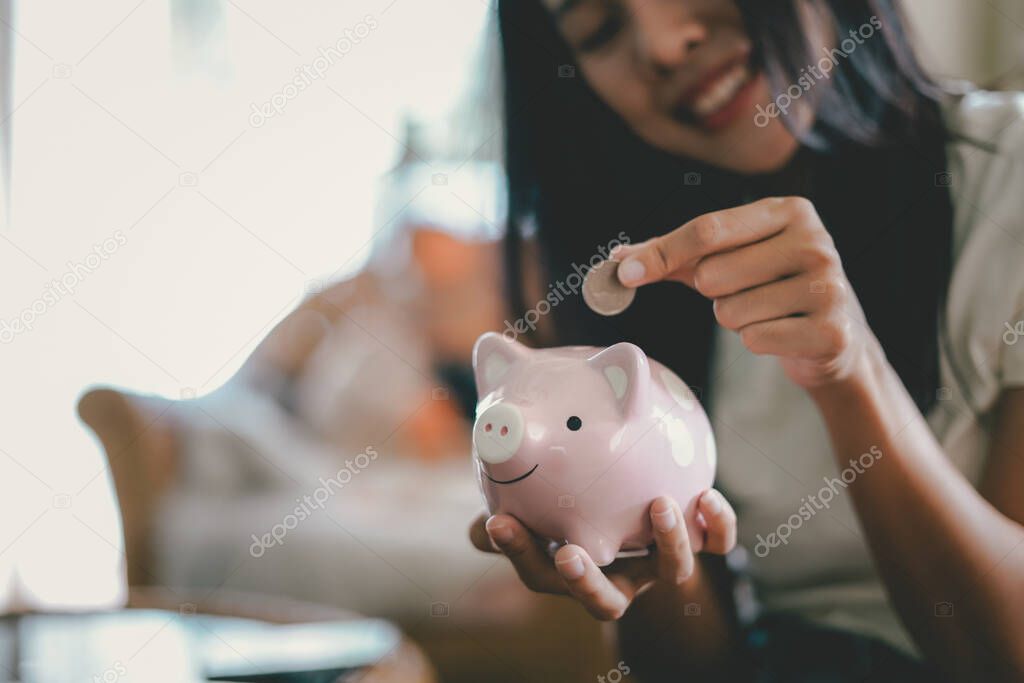 Happy young woman and hand putting coin into piggy bank, Finance or Savings concept.