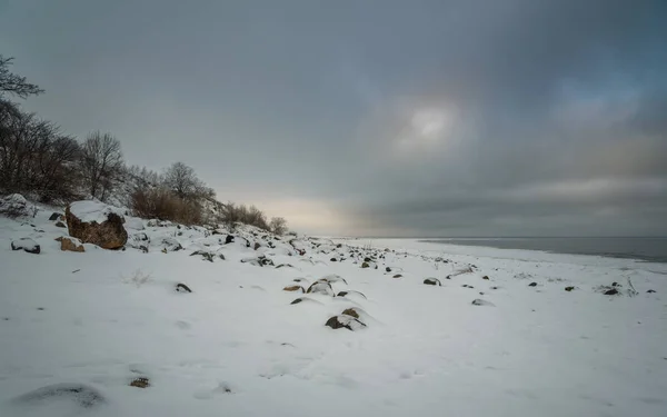 Snowy skalisty brzeg jeziora na tle szary zachmurzone niebo — Zdjęcie stockowe