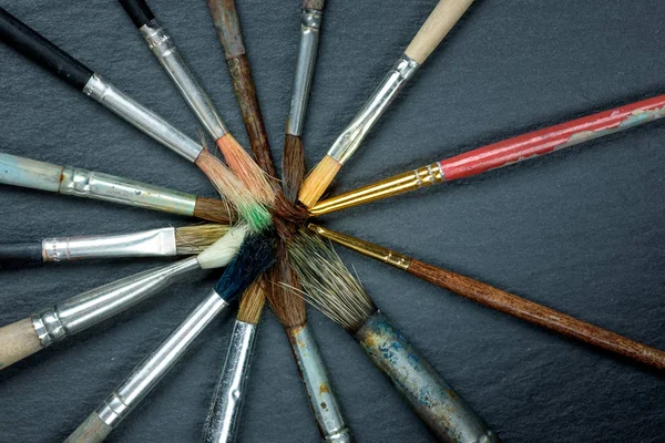 Used paint brushes laid out in a circle on dark background