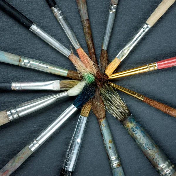 Used paint brushes laid out in a circle on dark background