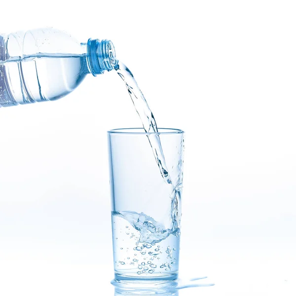 Gießen reinen klaren Wassers aus der Flasche in Glas auf weißem Hintergrund. — Stockfoto