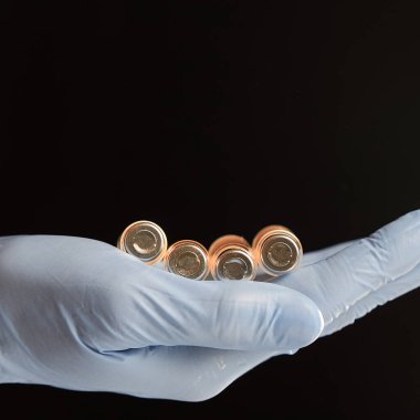 Mavi eldivenli el, siyah arka planda izole edilmiş birkaç şişe tutuyor..