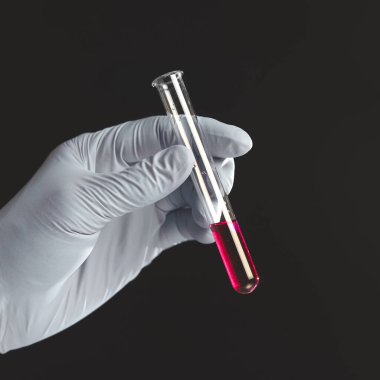 Deneme tüpünde kırmızı sıvıyı tutan el, siyah arkaplanda izole edilmiş..